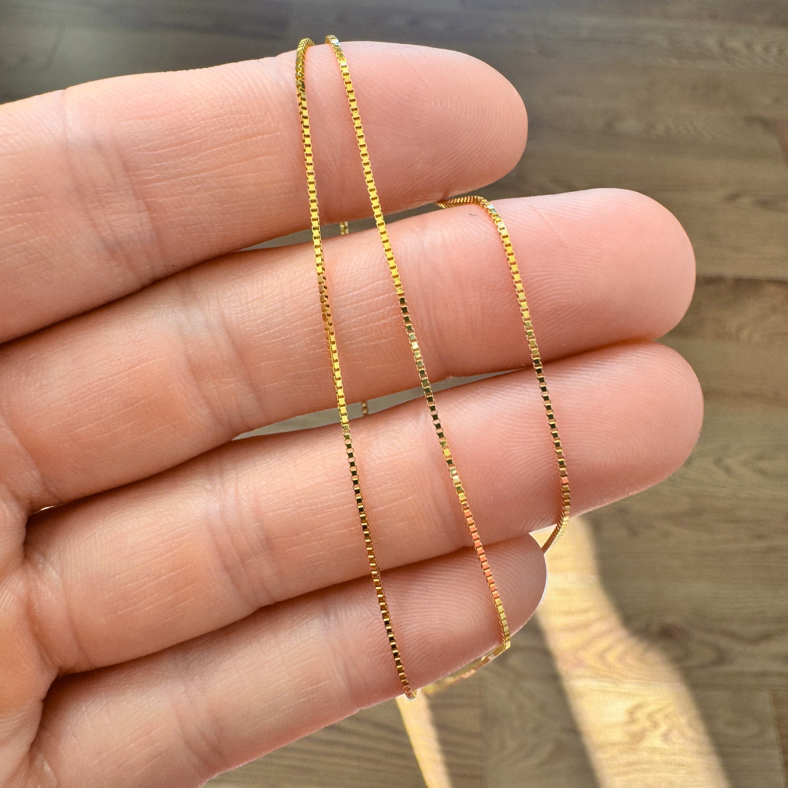 Gold chain held between fingers on a wooden surface