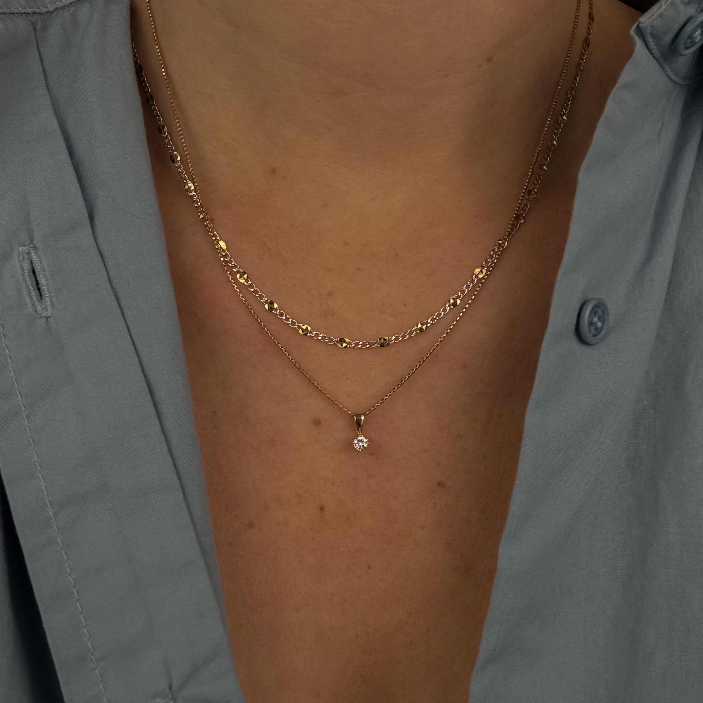 Gold necklace with a small pendant on a person wearing a light gray shirt.