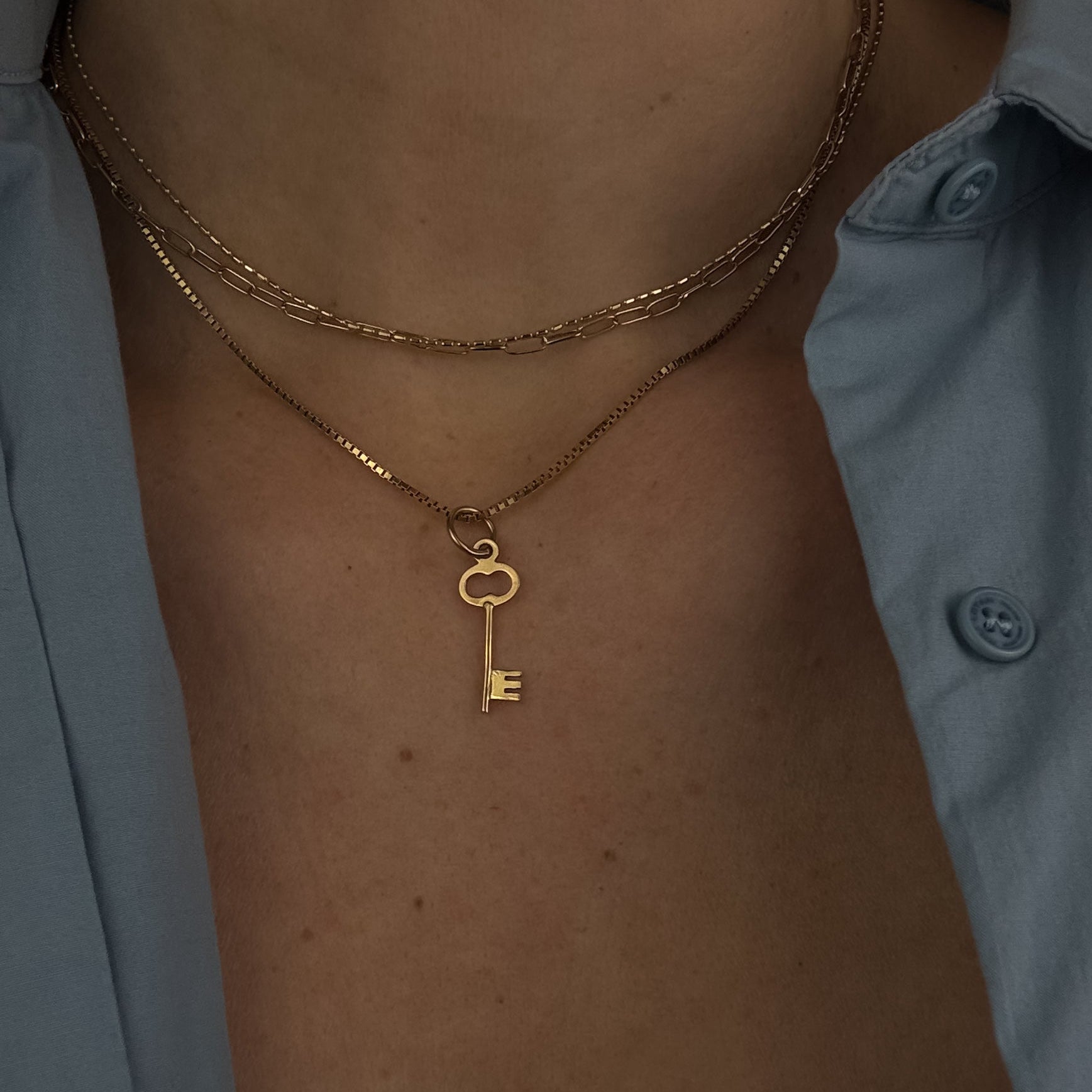 Gold key necklace on a person wearing a light blue shirt.