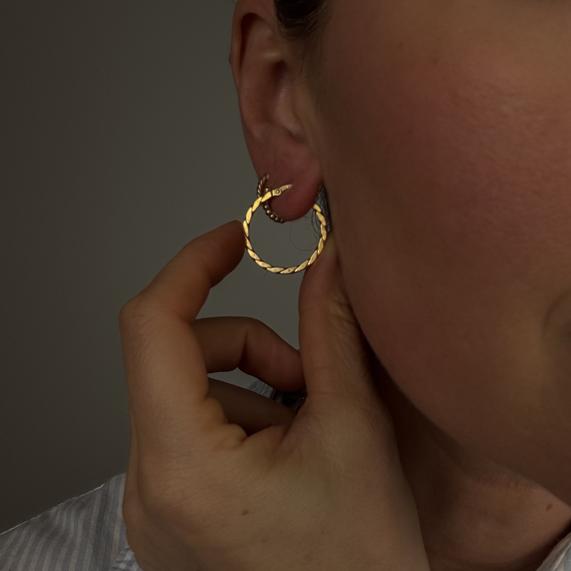 Gold hoop earring being worn and adjusted by a person with a neutral background