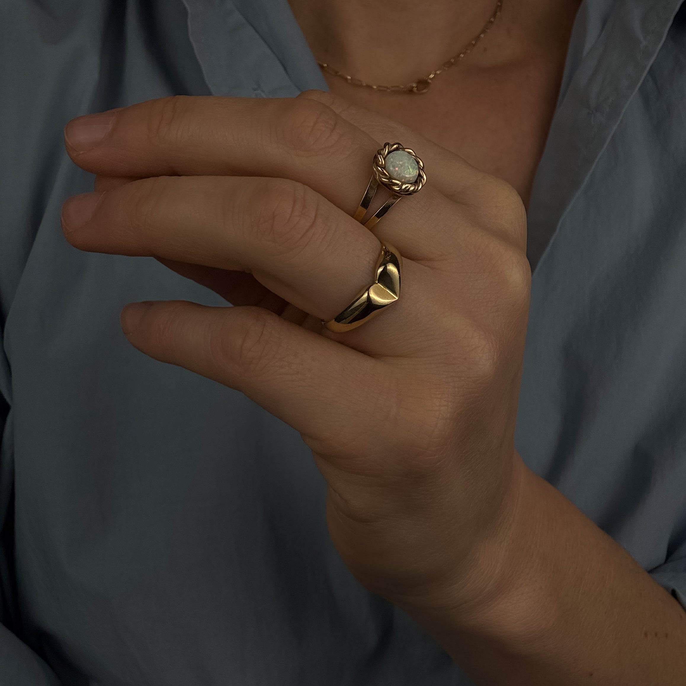 Close-up of a hand wearing two gold rings with a light blue shirt in the background