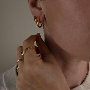 Close-up of a person wearing gold hoop earrings and rings.