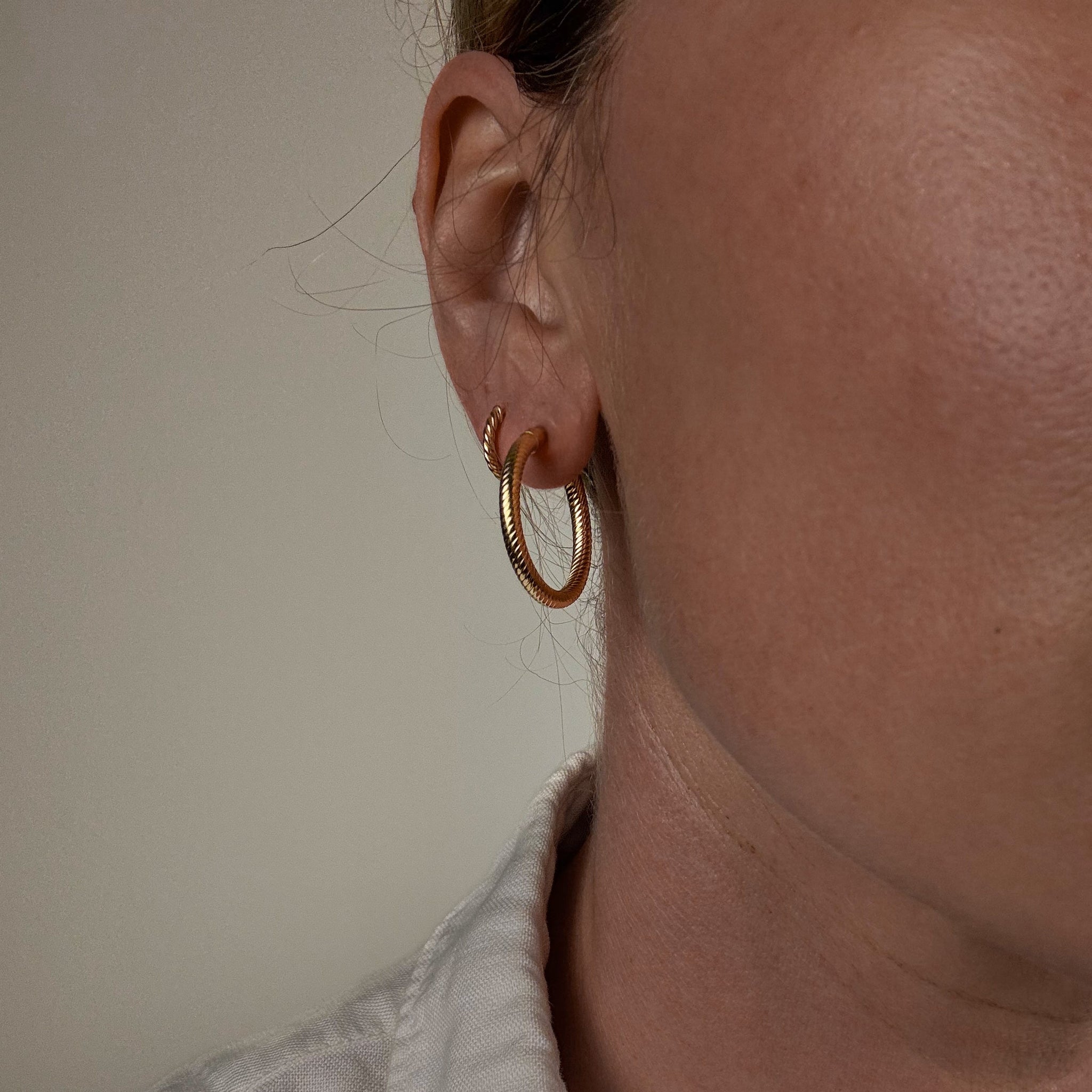 Close-up of a person wearing vintage folklor gold hoop earrings with a neutral background