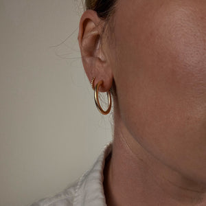 Close-up of a person wearing vintage folklor gold hoop earrings with a neutral background