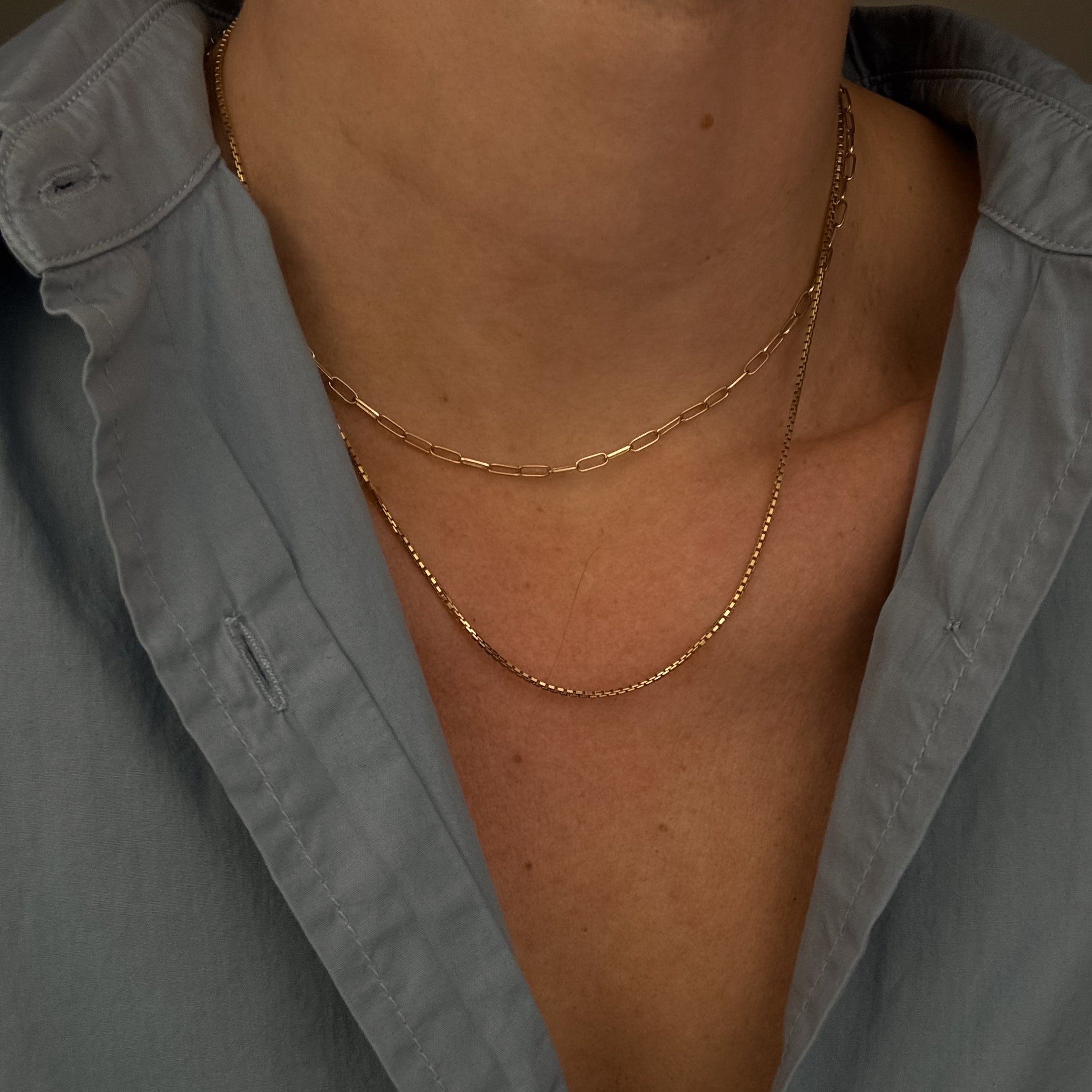 Close-up of a person wearing a gold necklace with an open light blue shirt.