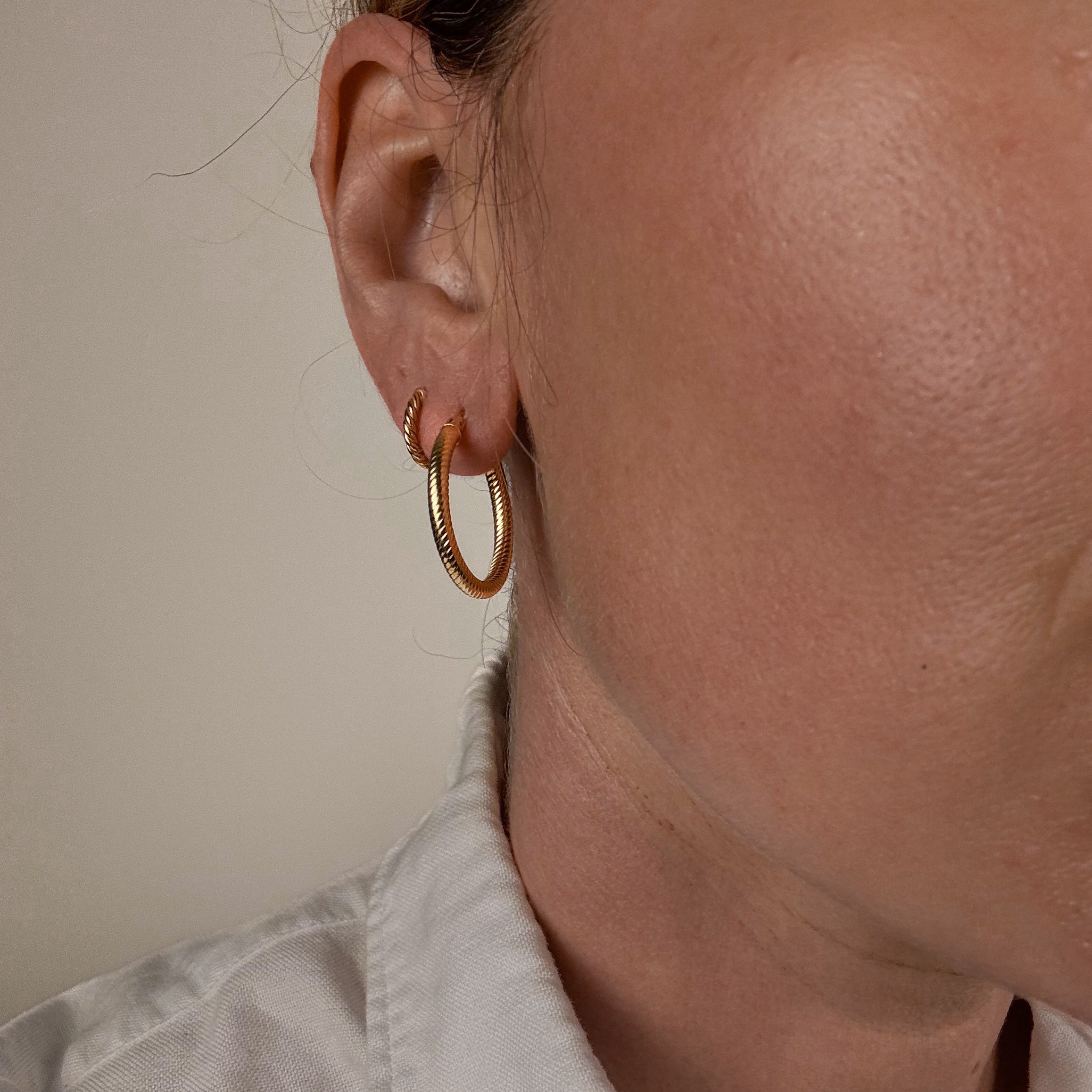 Close-up of a person wearing vintage folklor gold hoop earrings with a neutral background