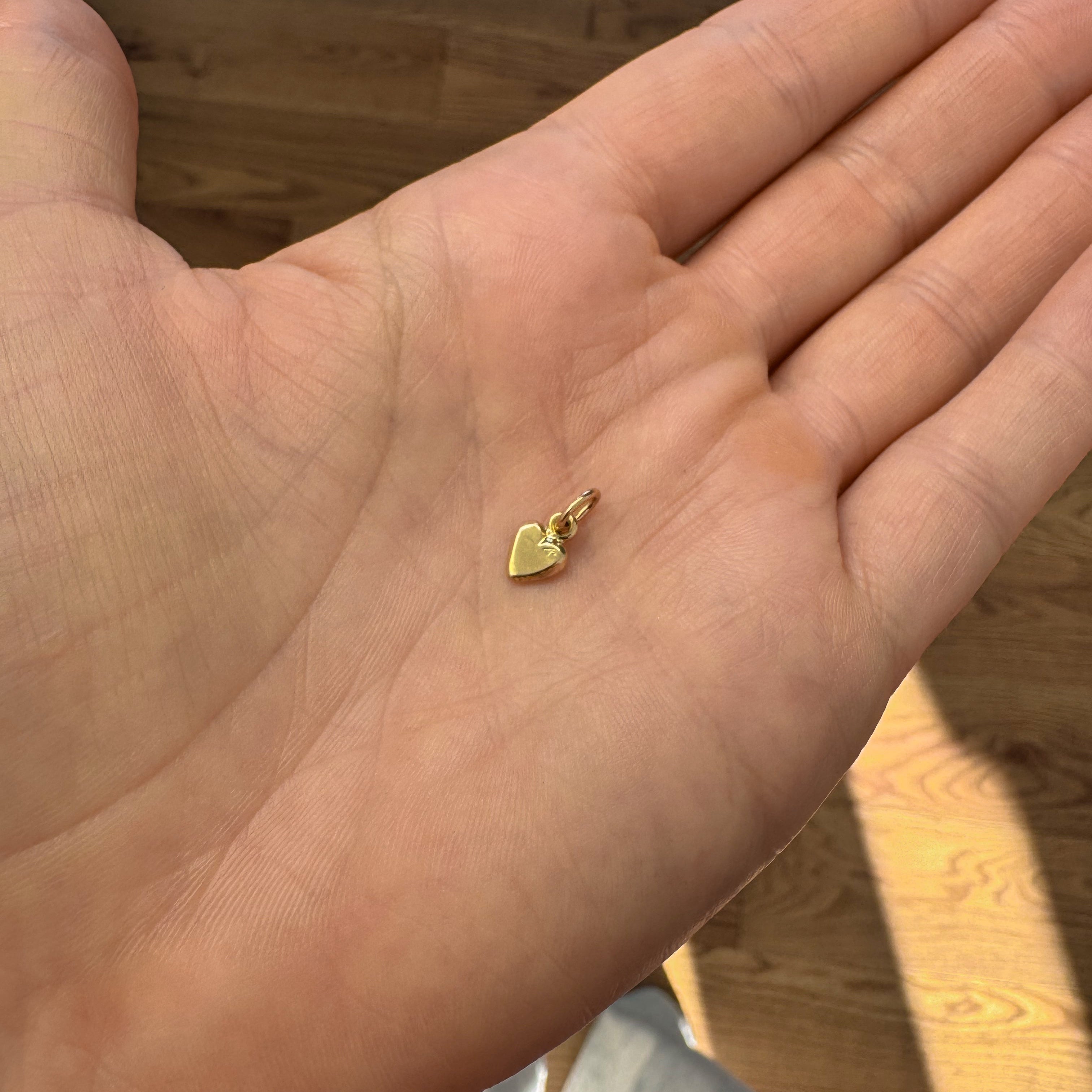 Hand holding a small gold heart-shaped pendant on a wooden floor background