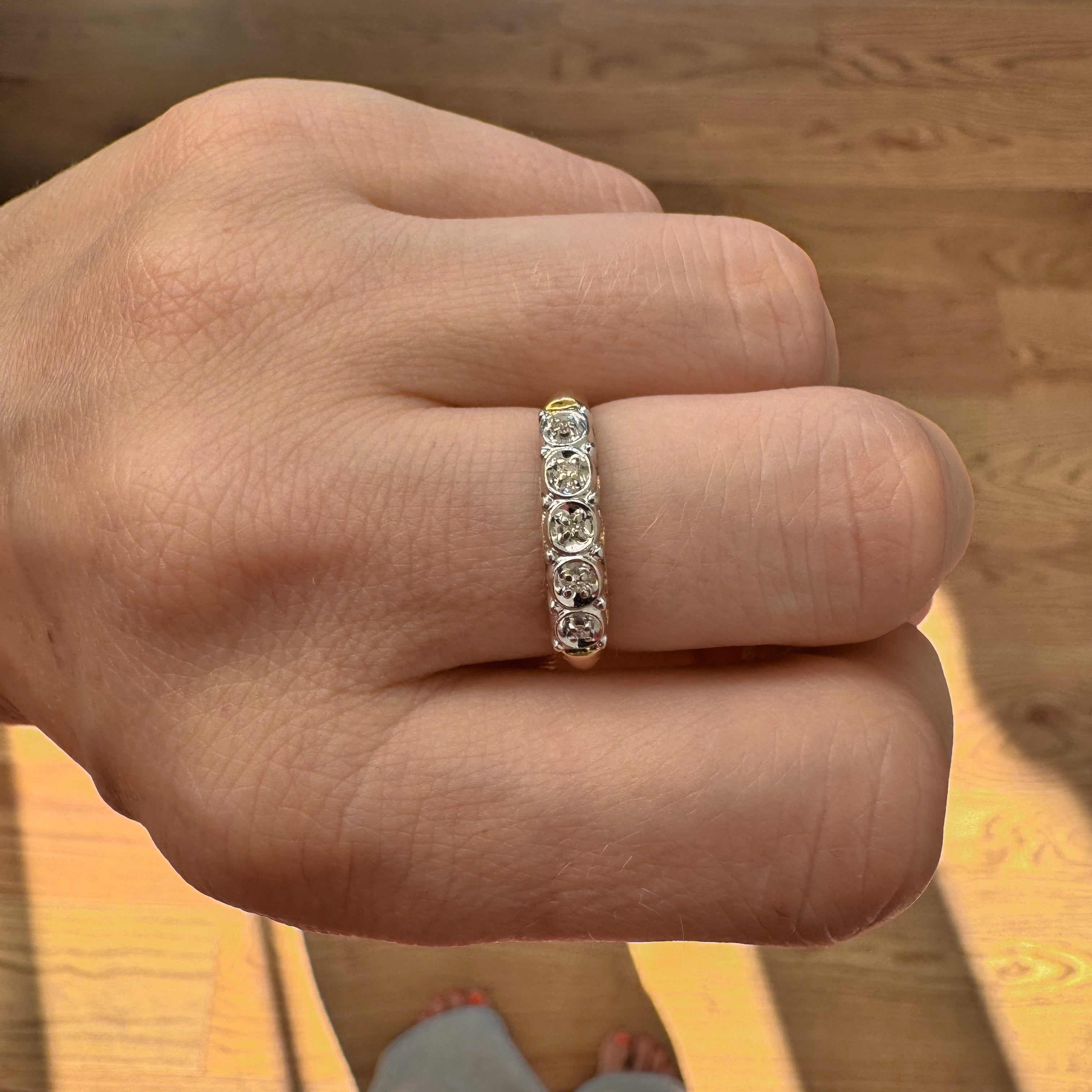 Hand wearing a diamond ring on a wooden floor