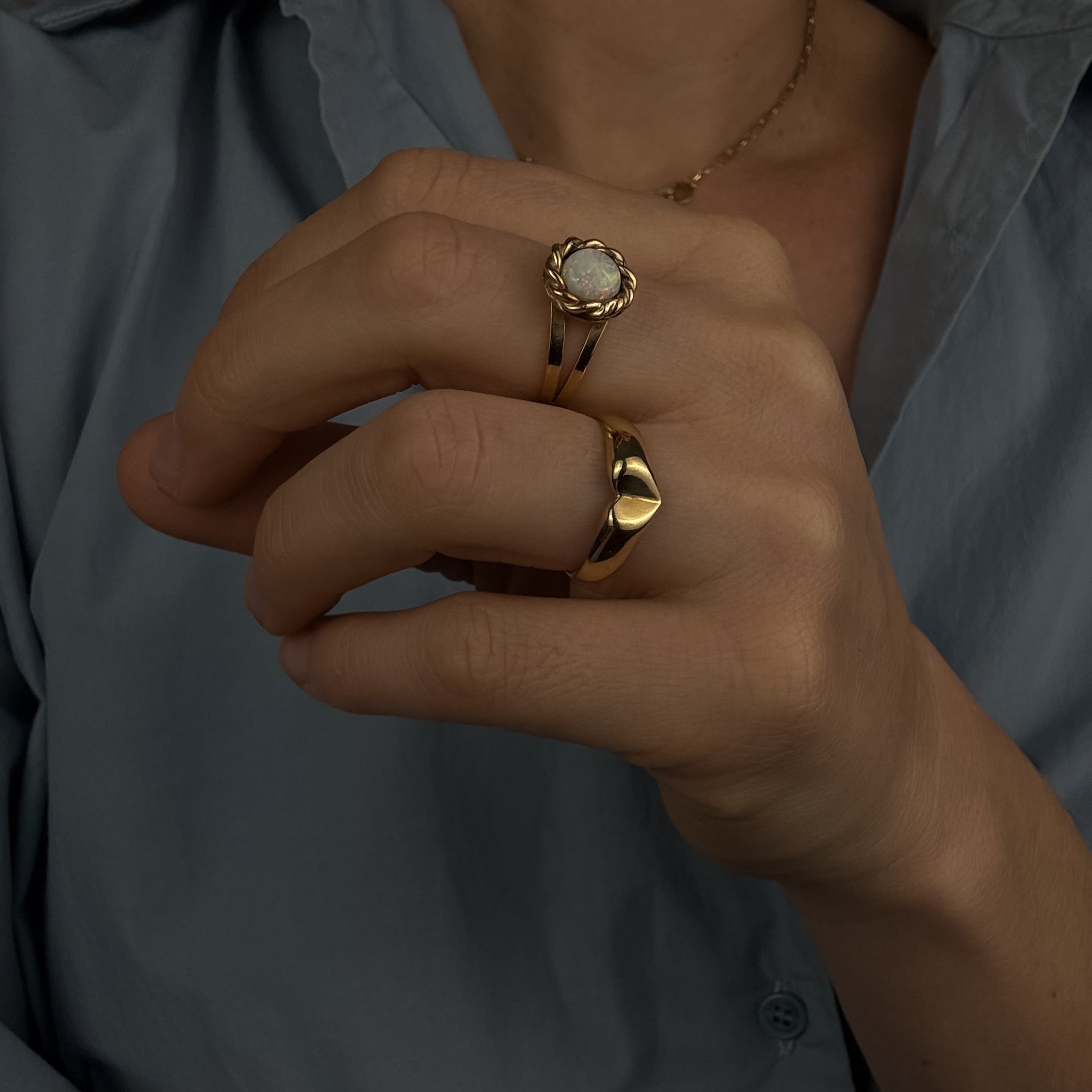 Close-up of a person wearing two gold rings with a light blue shirt.
