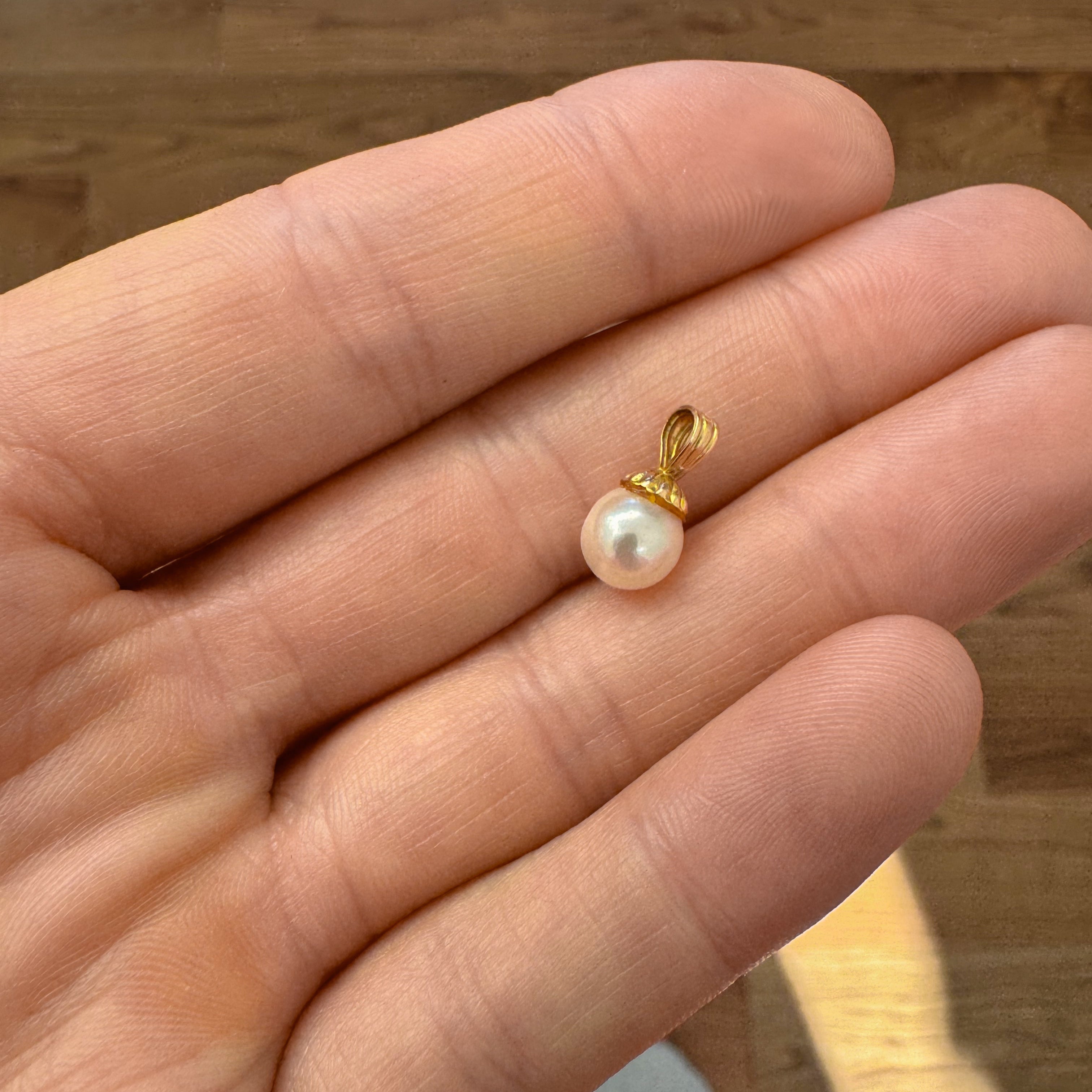 Gold pendant with a pearl held in a hand on a wooden surface