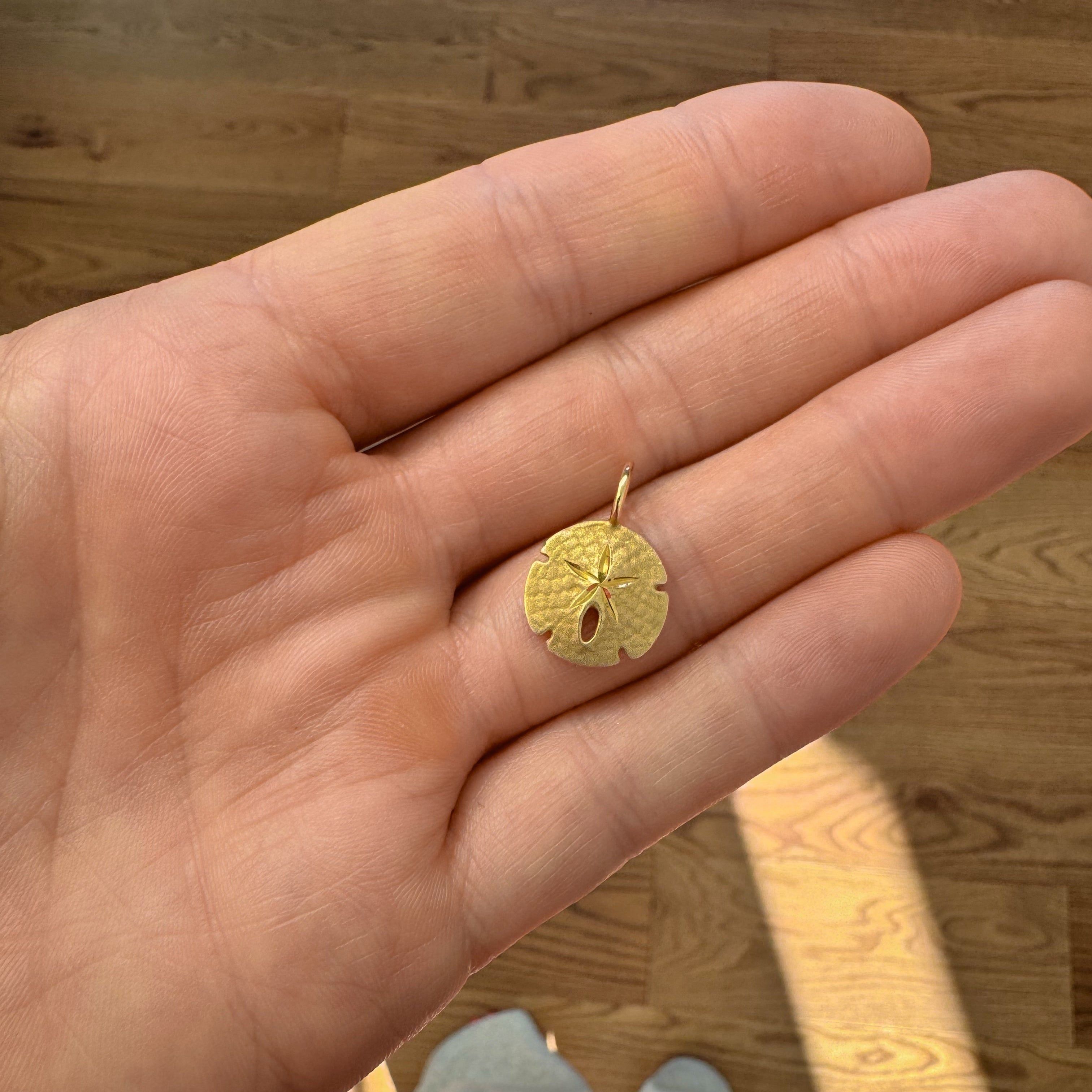 Gold pendant held in a hand on a wooden floor