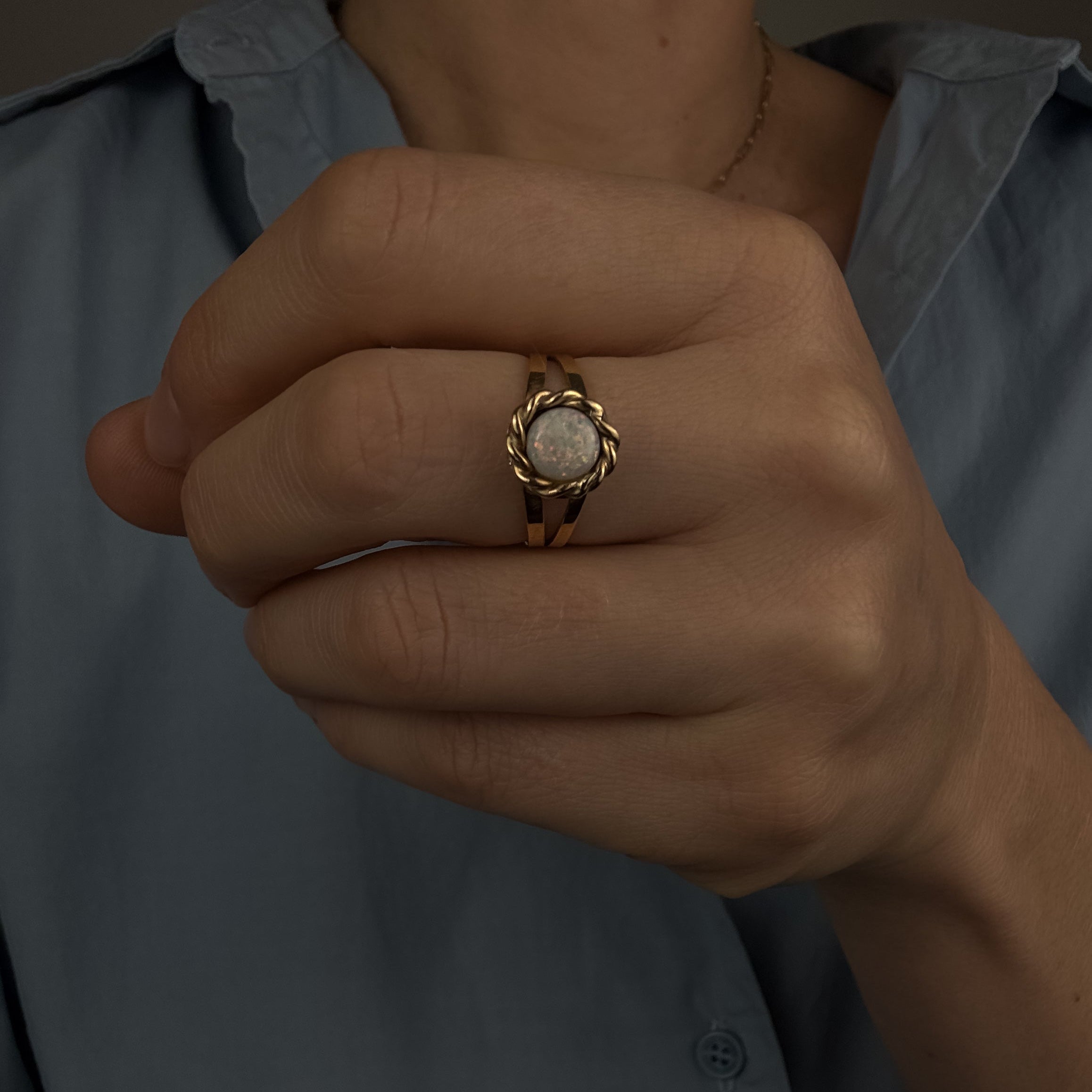 Close-up of a hand wearing a gold ring with a stone, against a neutral background.