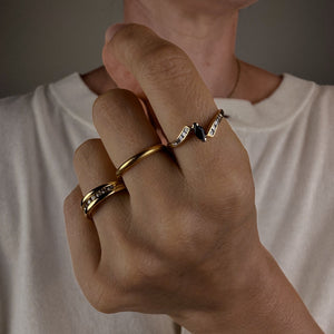 Hand wearing multiple gold rings with a neutral background
