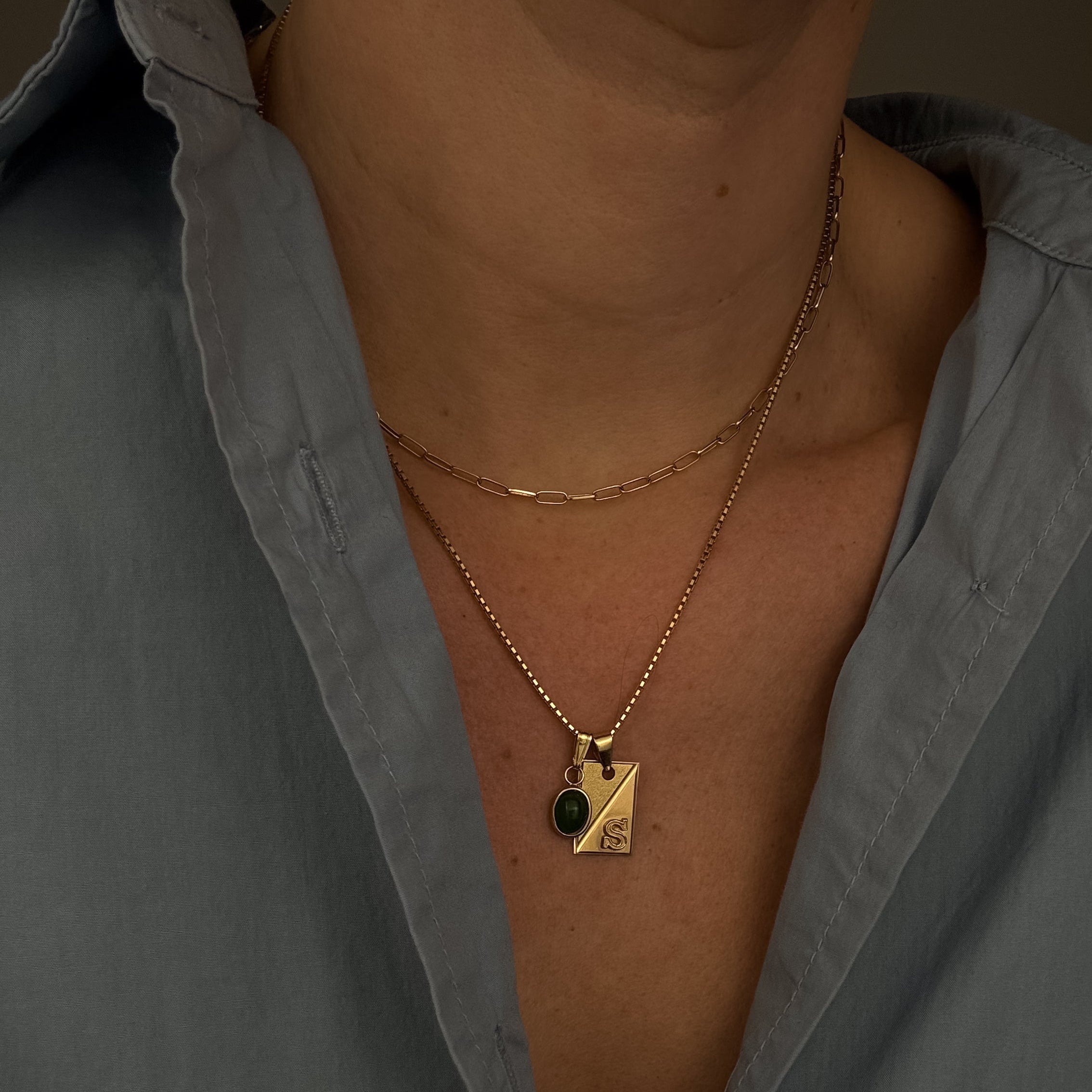 Close-up of a person wearing a gold necklace with a pendant against a gray shirt.