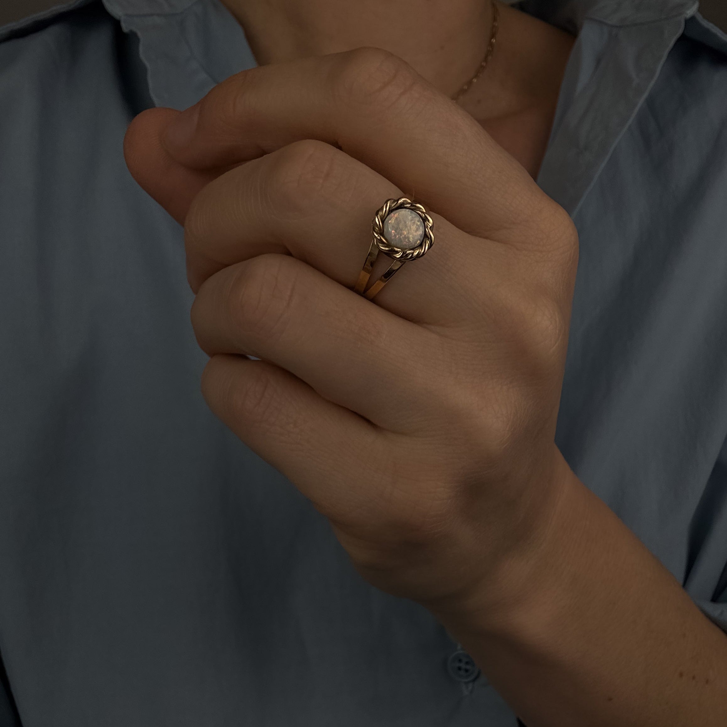 Close-up of a hand wearing a gold ring with a diamond, against a blurred background.