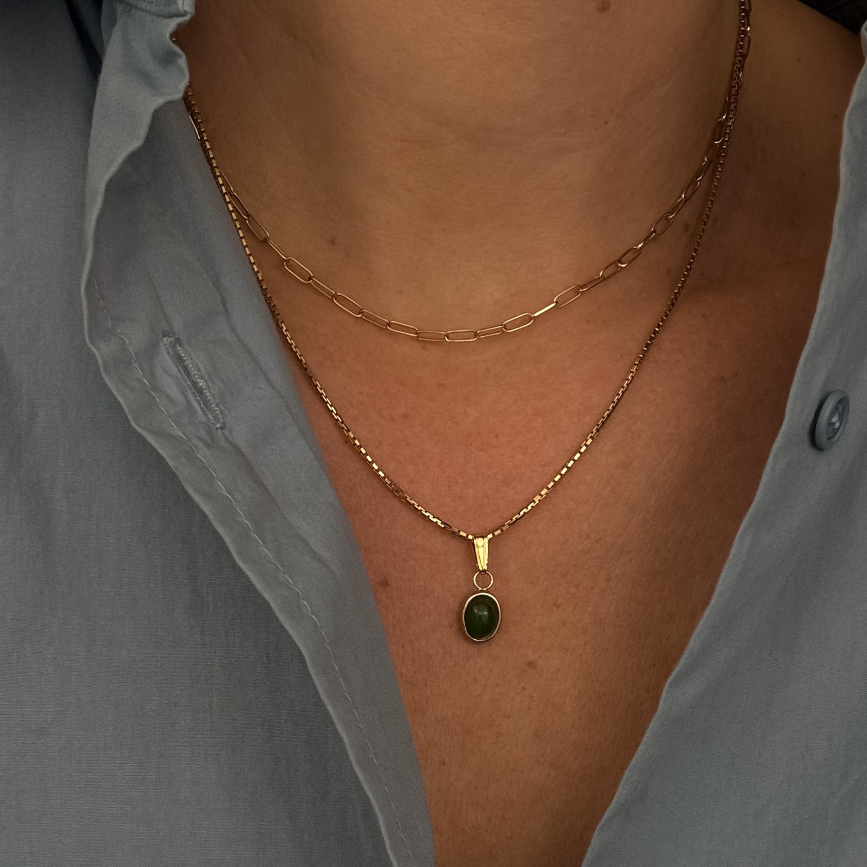 Necklace with a green pendant worn by a person in a light gray shirt.