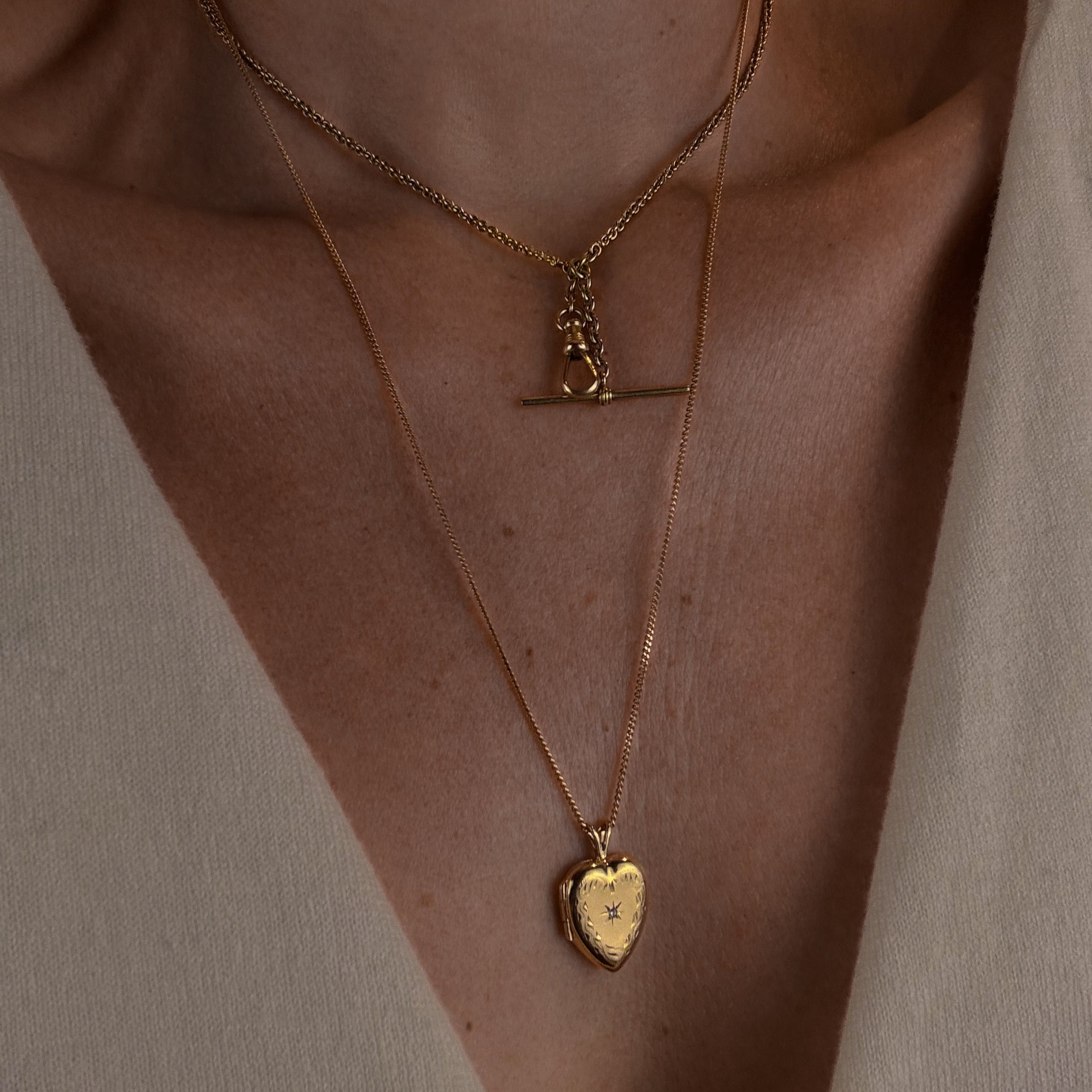 Close-up of a person wearing two gold necklaces with pendants on a neutral background
