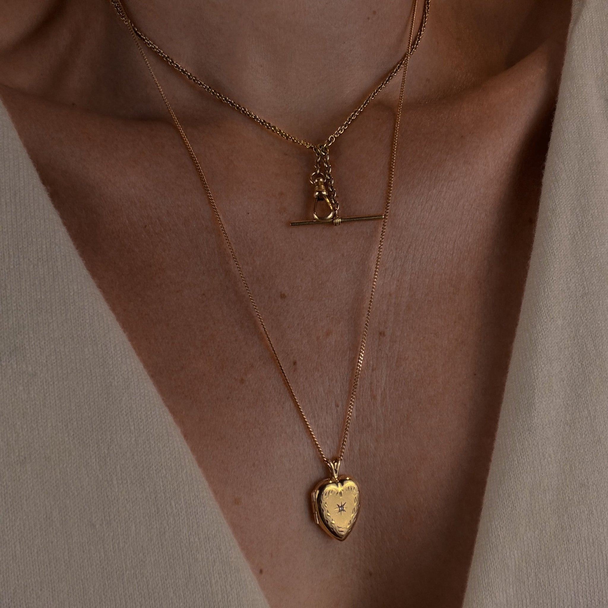 Close-up of a person wearing two gold necklaces with pendants on a neutral background