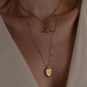 Close-up of a person wearing two gold necklaces with pendants on a neutral background