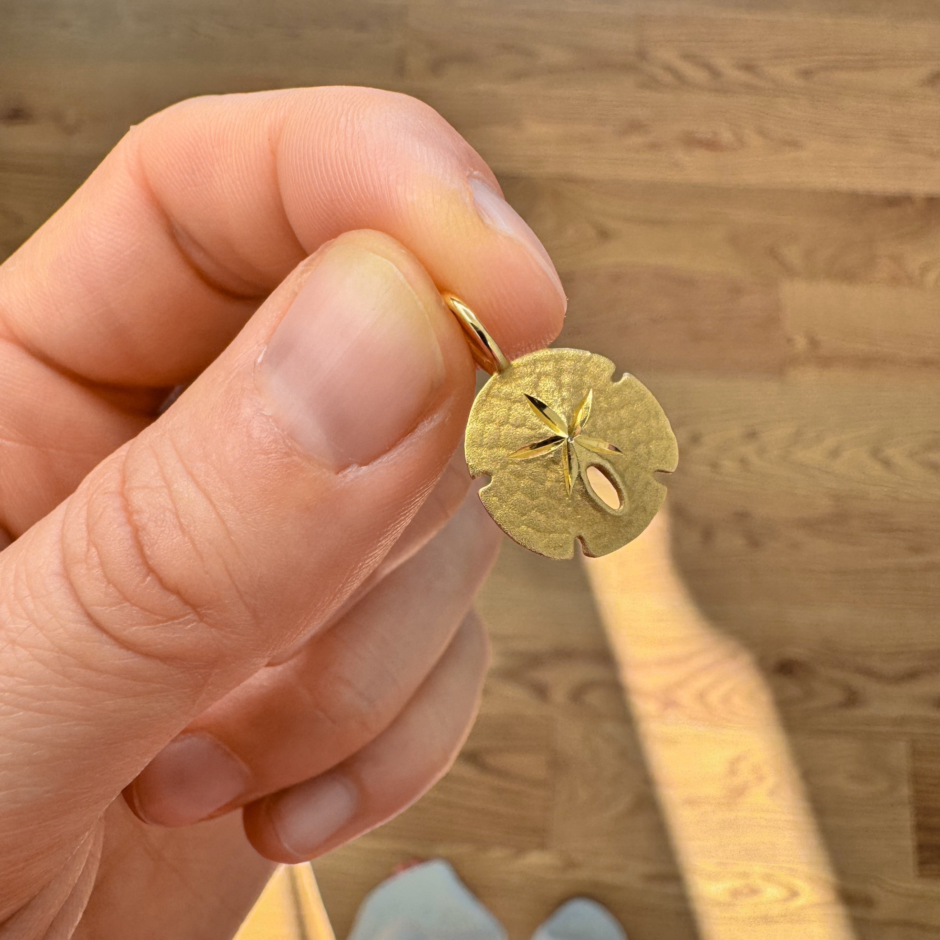 Hand holding a gold sand dollar pendant against a wooden background