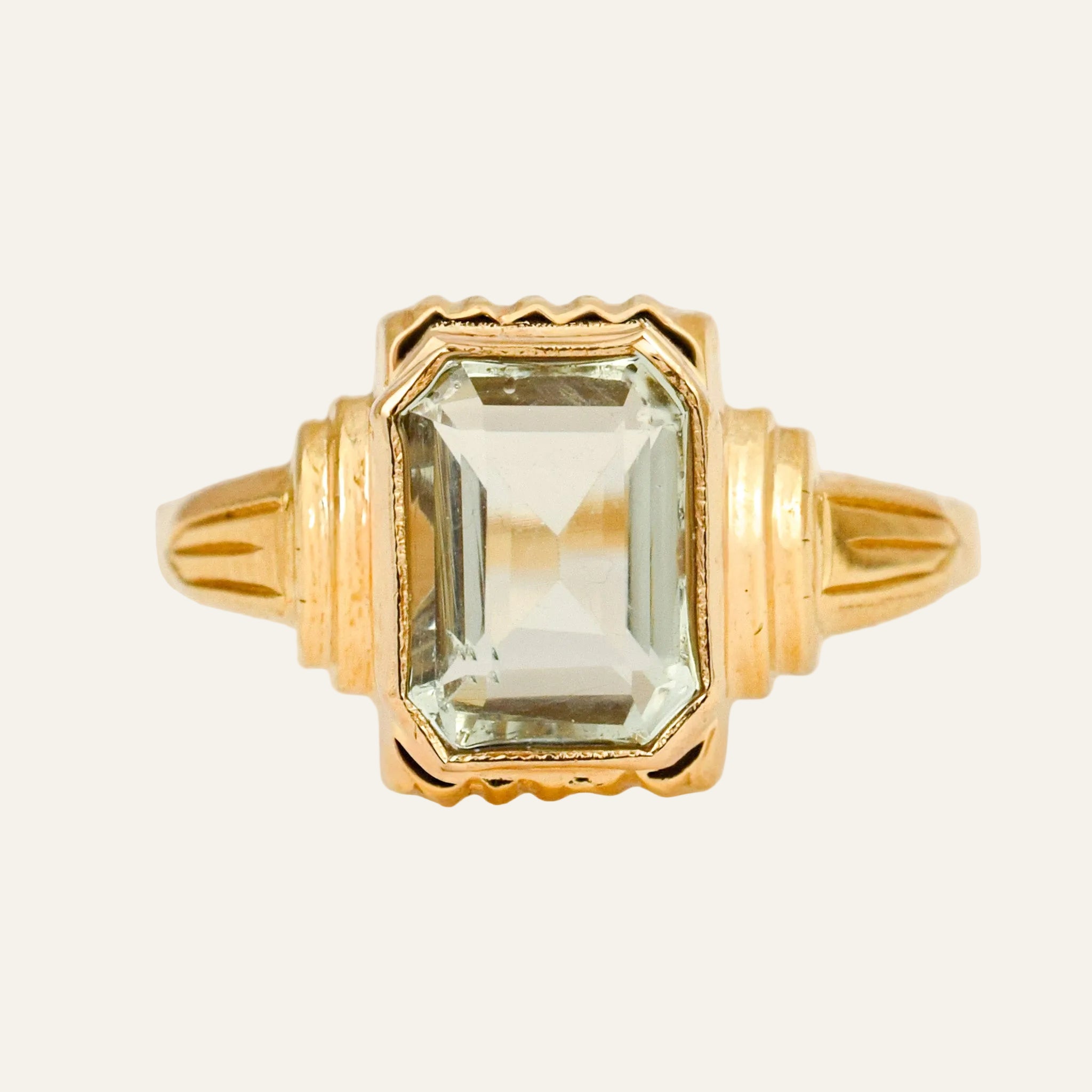 Emerald-cut pale green amethyst bezel-set in an ornate 10k yellow gold ring with scalloped edges and stepped ribbed shoulders