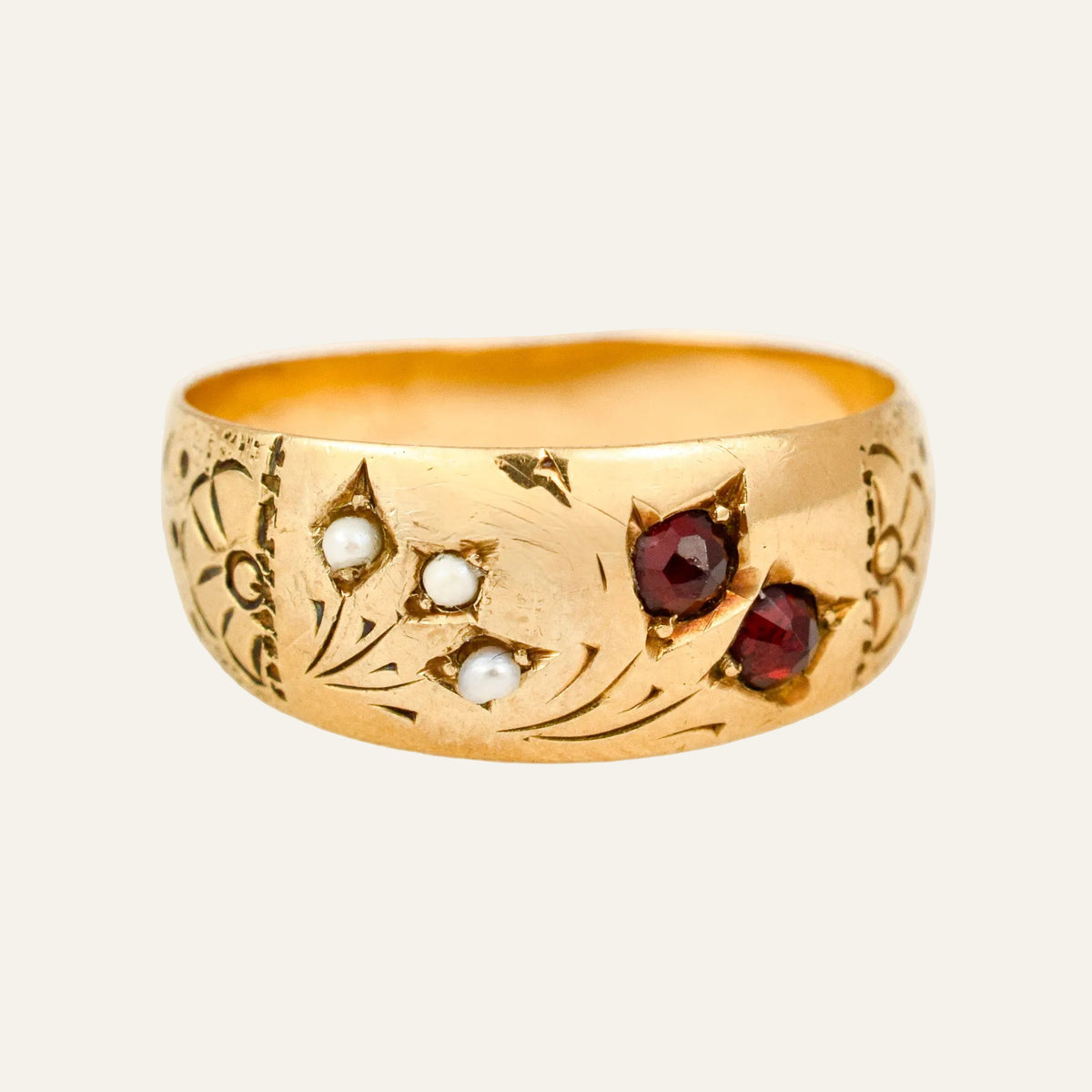 Antique 10k gold band with garnets and seed pearls star-set flush into the domed gold, with engraved floral shoulders.