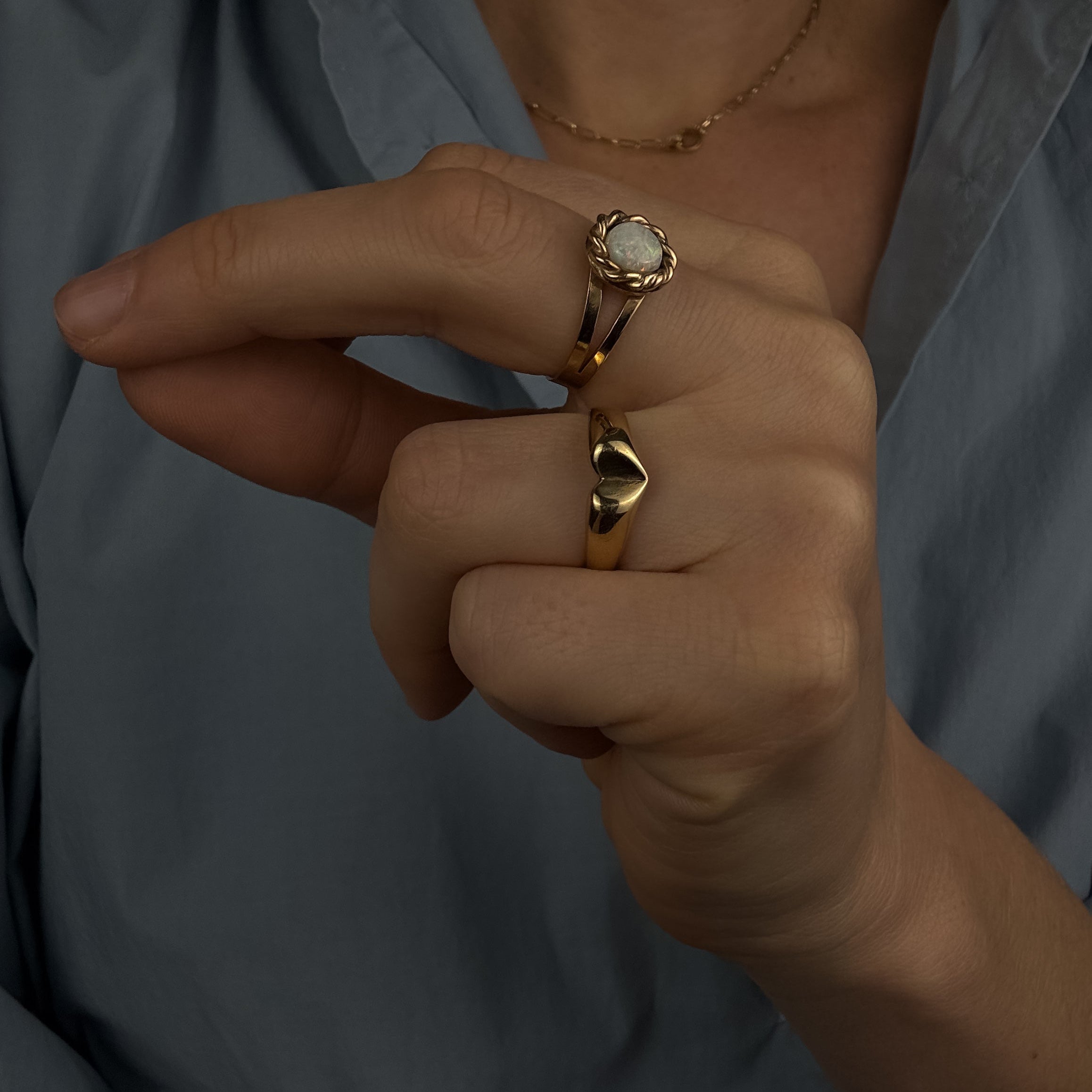 Close-up of a person wearing two gold rings with a light blue shirt in the background