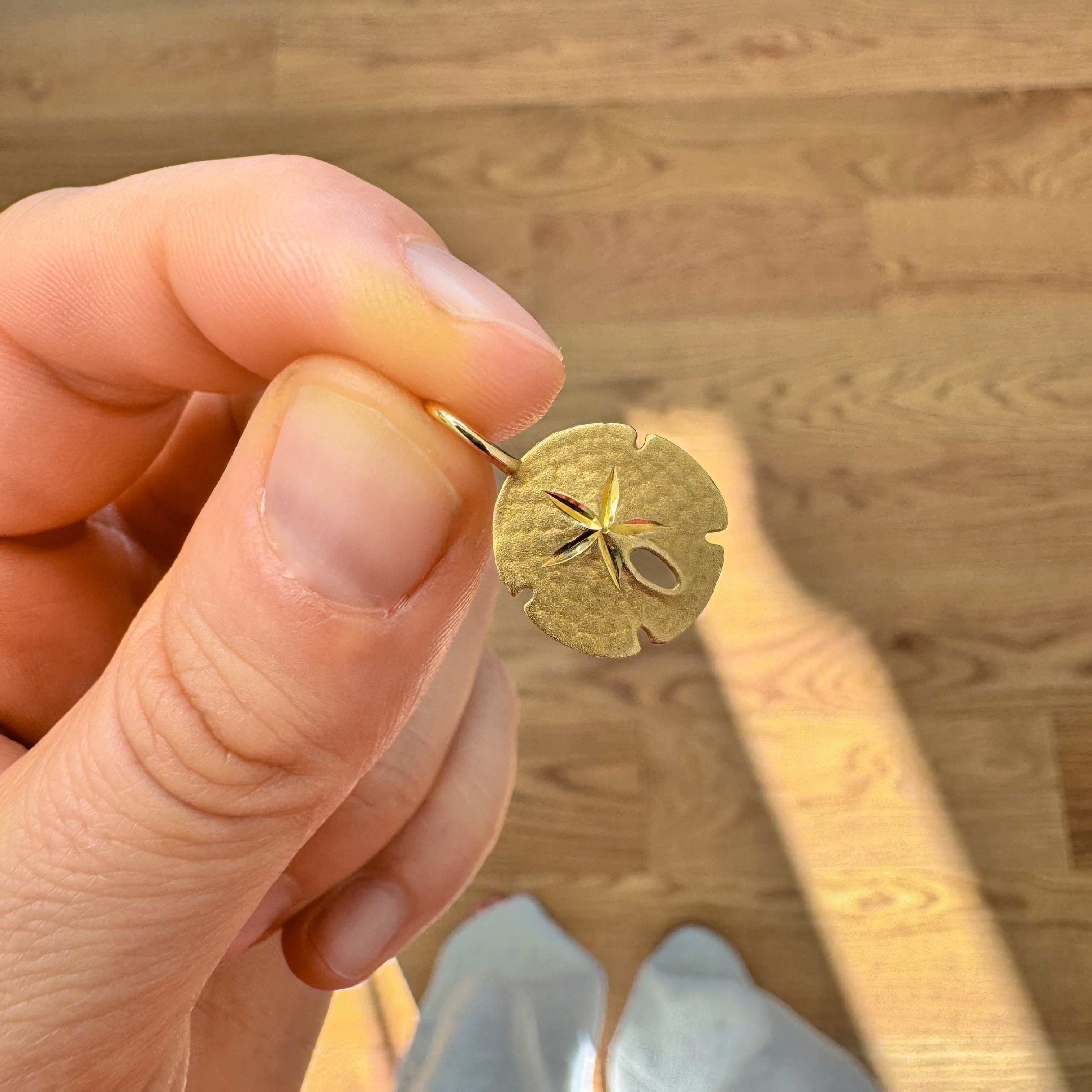 Hand holding a gold sand dollar pendant against a wooden floor background