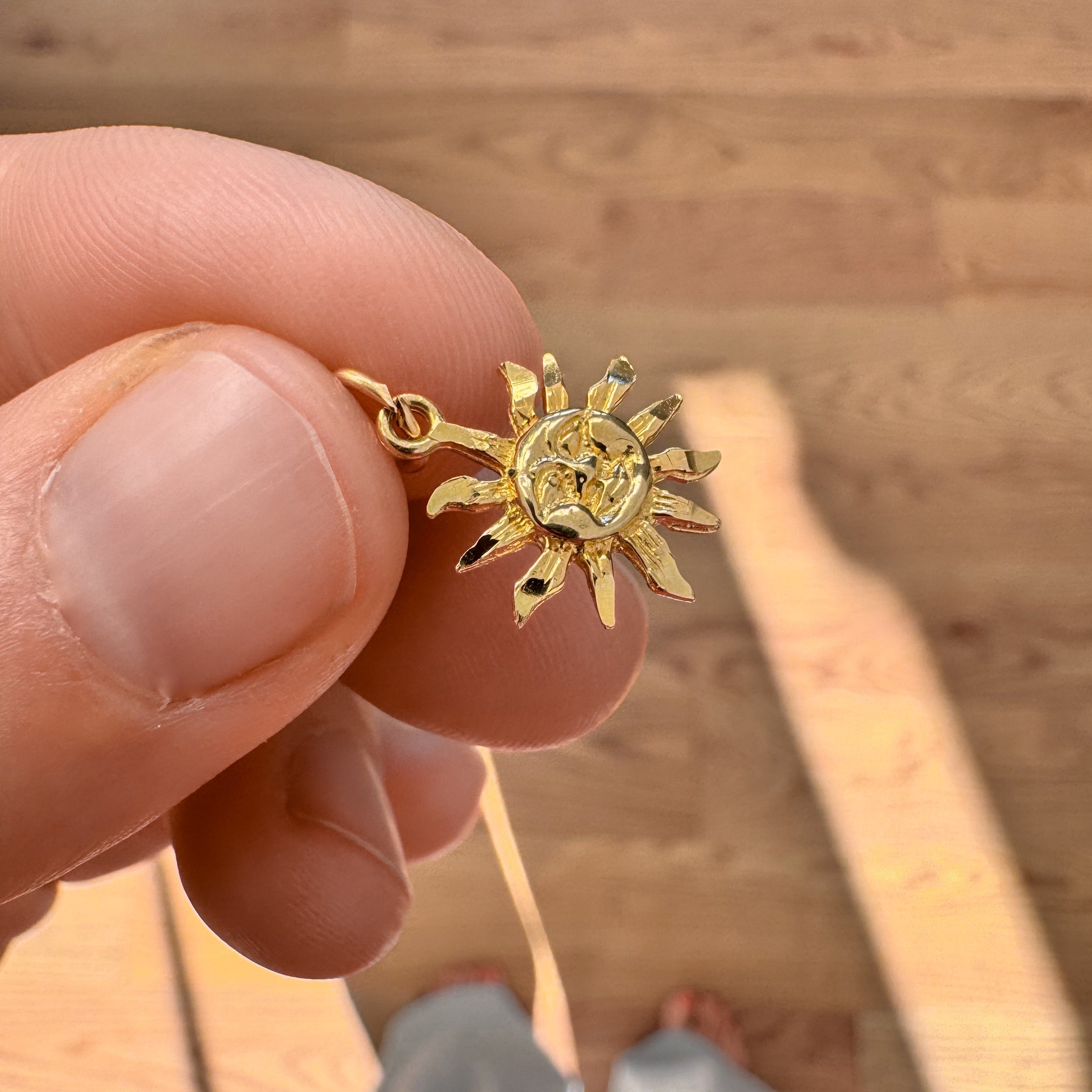 Gold sun-shaped pendant held by a hand on a wooden floor.