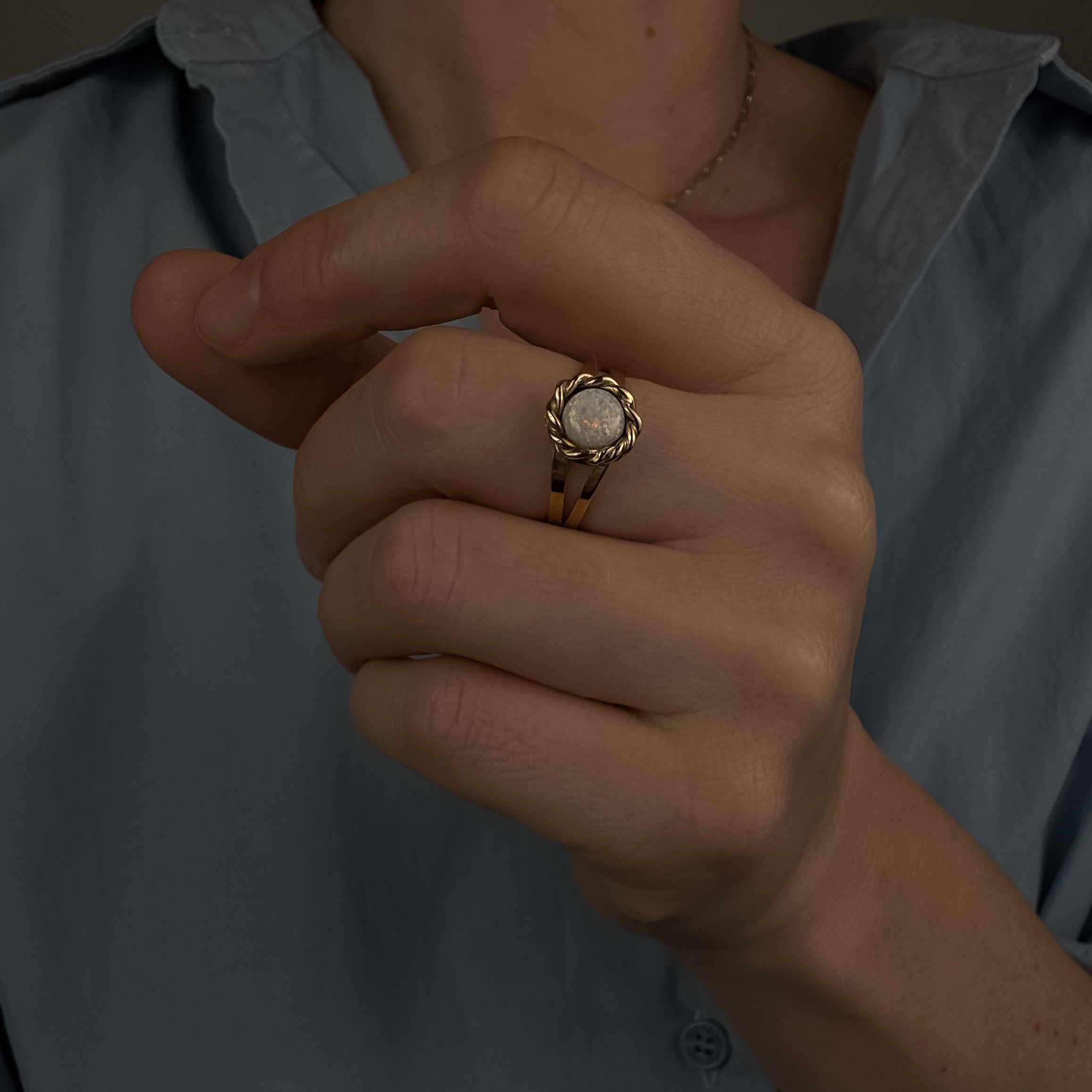 Close-up of a hand wearing a gold ring with a diamond, against a blurred background.