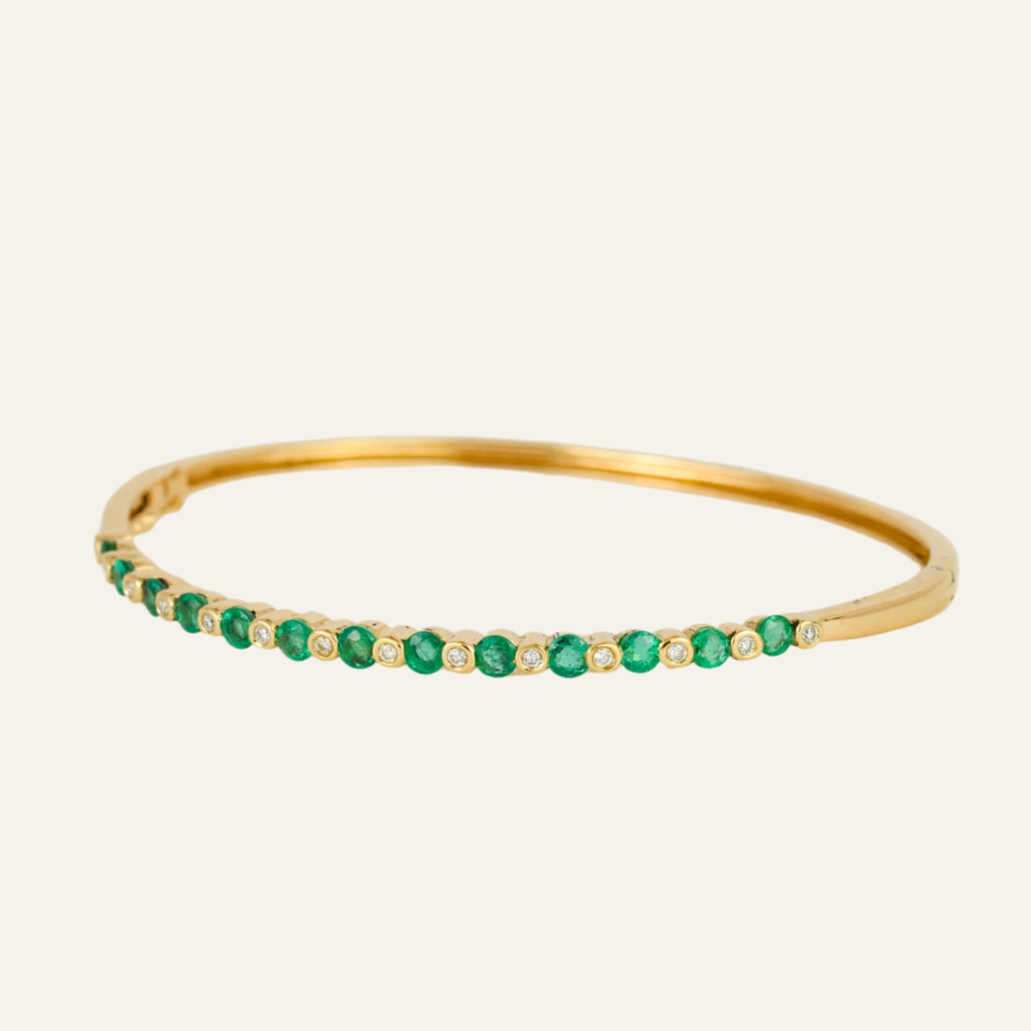 Gold bracelet with emeralds and diamonds on a light gray background