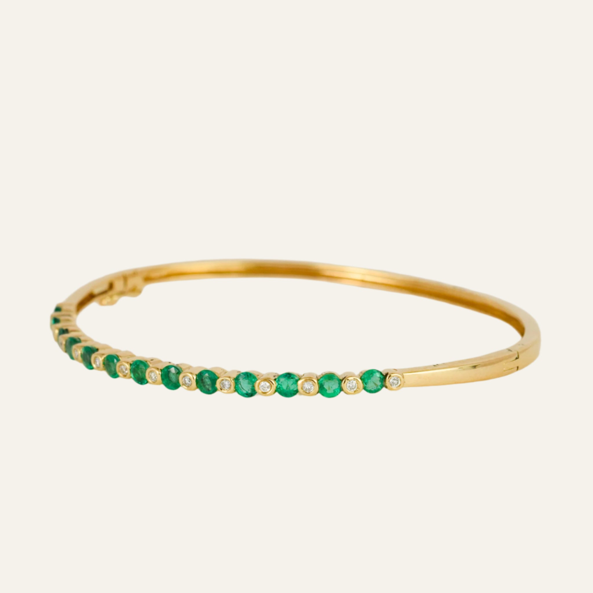 Gold bracelet with emeralds and diamonds on a light gray background
