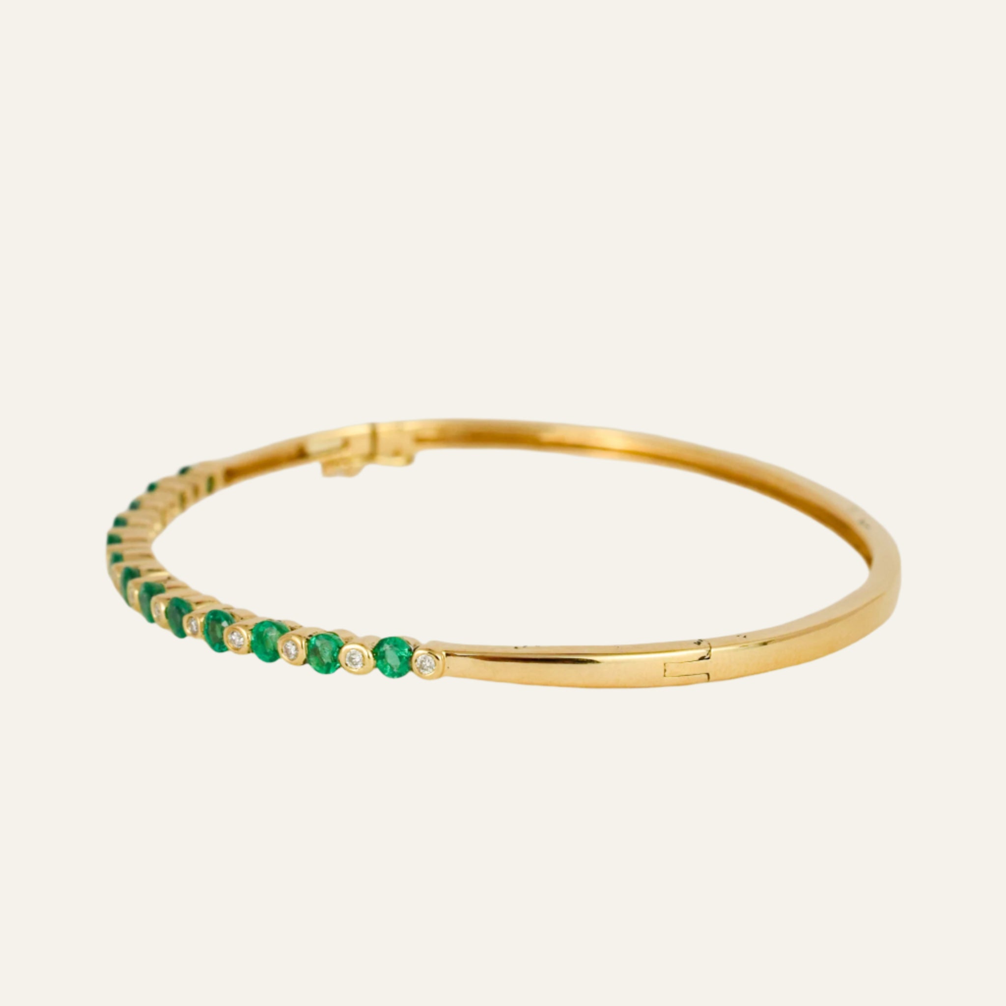 Gold bracelet with emeralds and diamonds on a light gray background