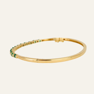 Gold bracelet with emeralds and diamonds on a light gray background