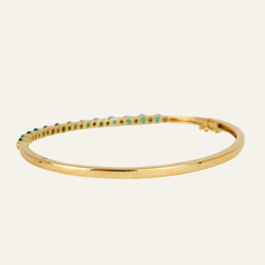 Gold bracelet with emeralds and diamonds on a light gray background