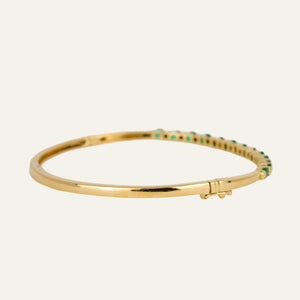 Gold bracelet with emeralds and diamonds on a light gray background