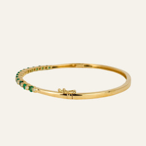 Gold bracelet with emeralds and diamonds on a light gray background