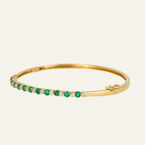 Gold bracelet with emeralds and diamonds on a light gray background