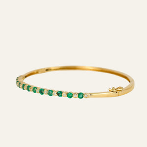 Gold bracelet with emeralds and diamonds on a light gray background