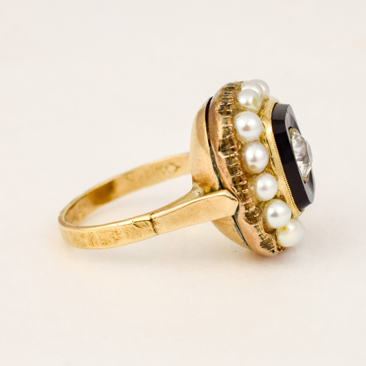 Profile view of a Victorian 10k gold onyx mourning ring showing the pearl surround and plain tapered shank.