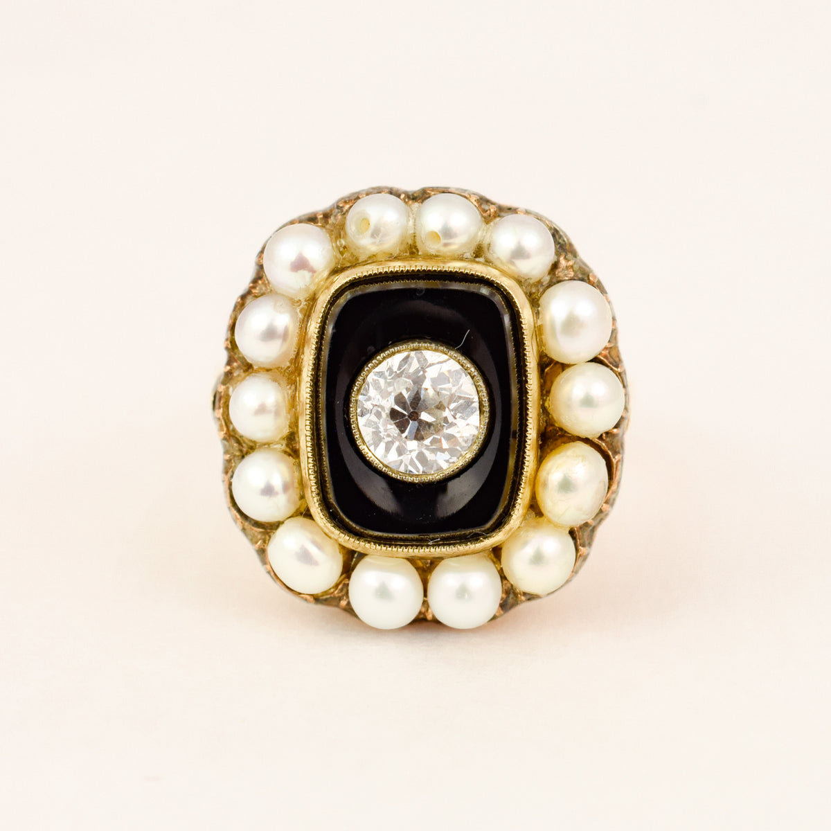 Top view of a Victorian onyx mourning ring, old mine cut diamond bezelled in the onyx panel within fourteen pearls.