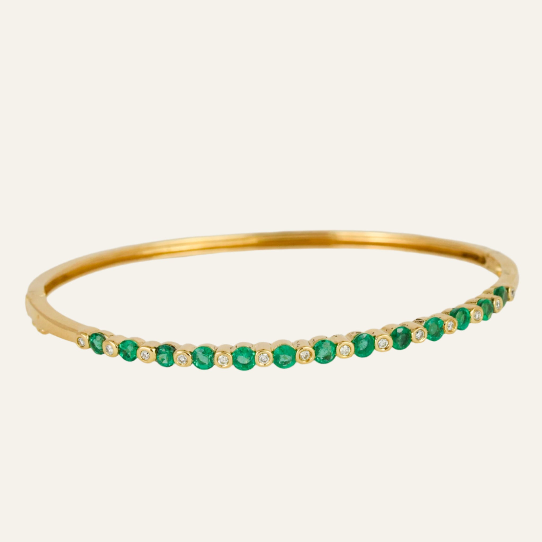 Gold bracelet with emeralds and diamonds on a light gray background