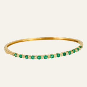 Gold bracelet with emeralds and diamonds on a light gray background