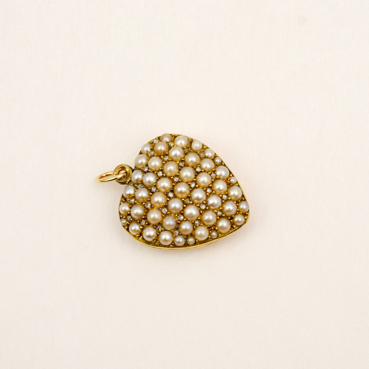 Angled view of a 1912 English 9k gold heart locket showing seed pearls and diamonds across the face.